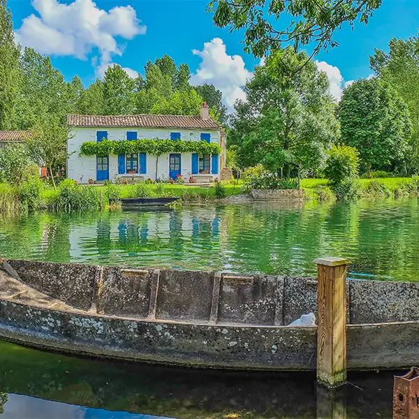Maison aux volets bleus et barque sur un canal du Marais Poitevin