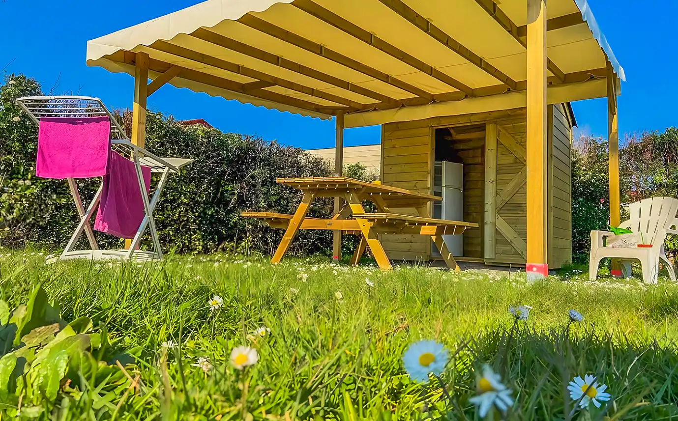 Espace couvert d’un emplacement Privilège Garden avec table en bois, réfrigérateur et étendoir, en Vendée