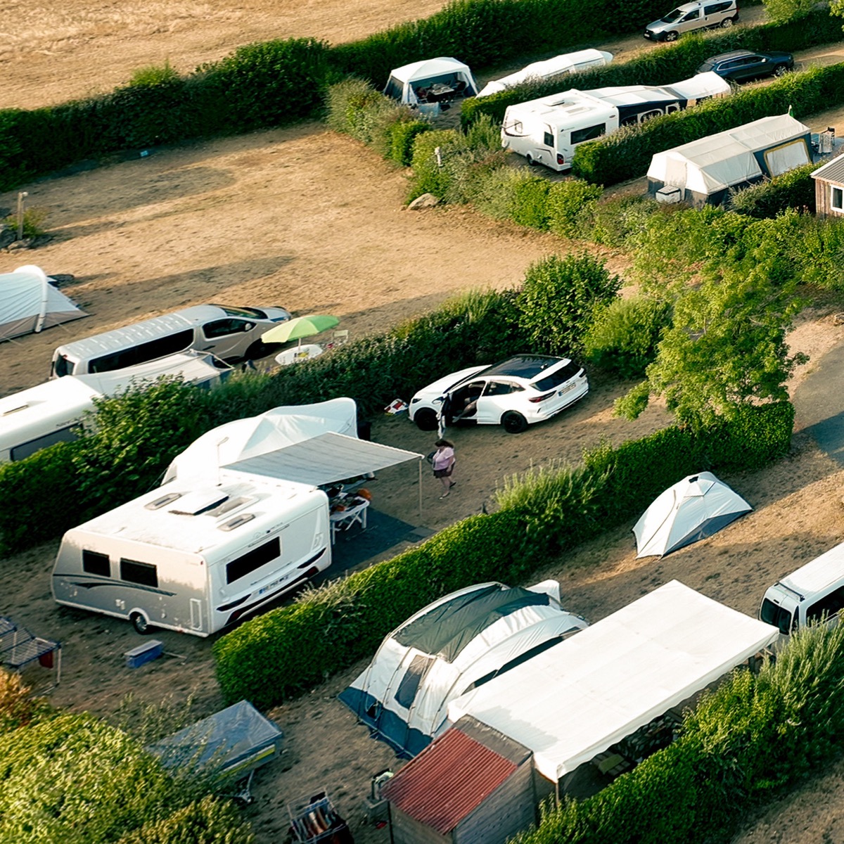 Emplacements délimités par des haies avec caravanes, camping-cars et tentes au camping en Vendée